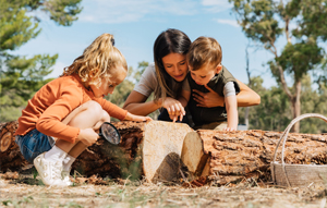 Mother and little boy and girl playing obn a tree trunk