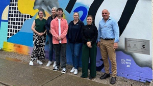 Four casually dressed people standing against a graffiti mural