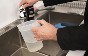 A jug being filled from a tap by a man wearing a black long sleeved top