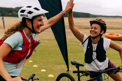 Two young females high fiving each other while sat on bikes at the finish line of a race
